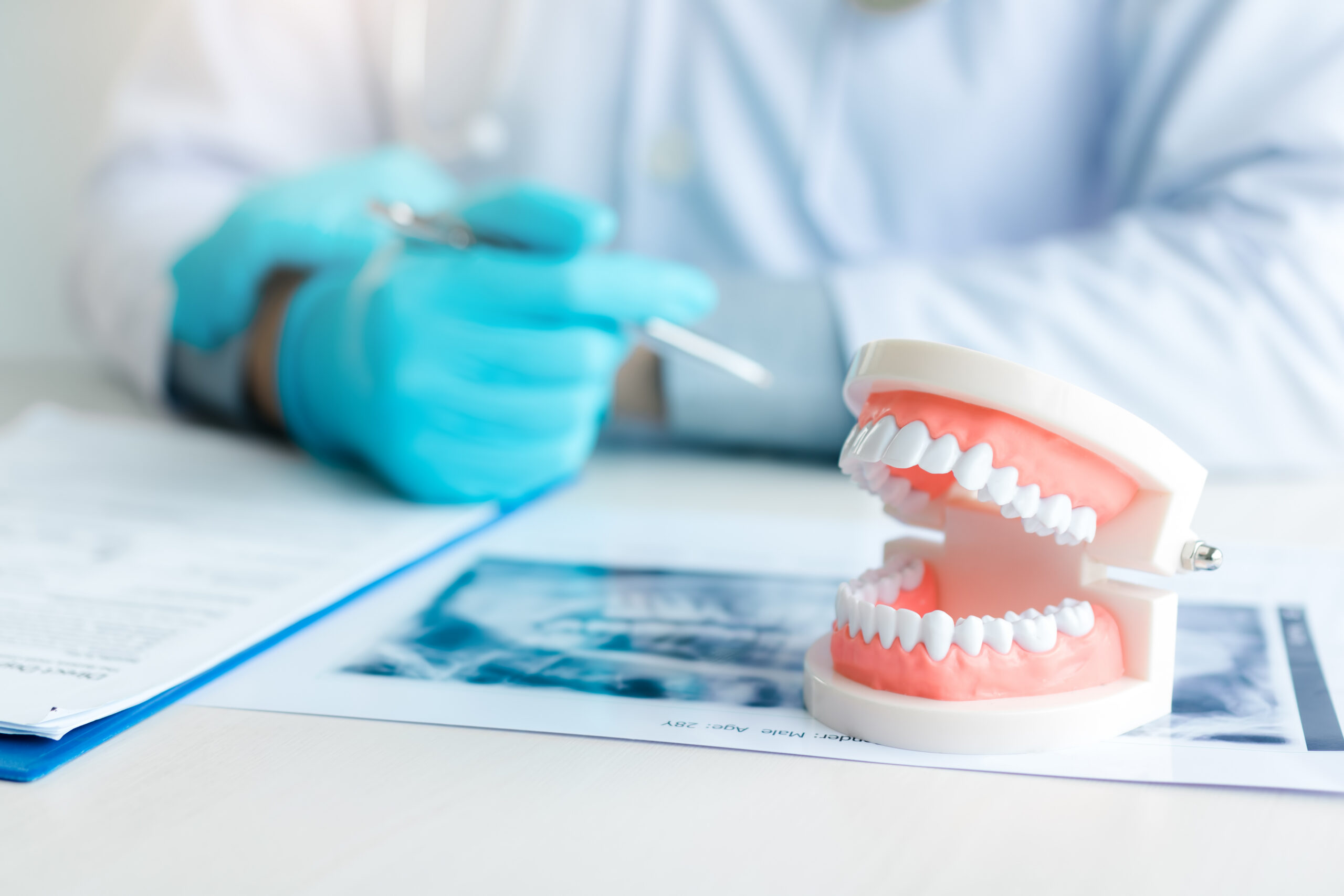 A dentist sits at a desk. A physical model of dentures sits on the desk on top of X-ray images