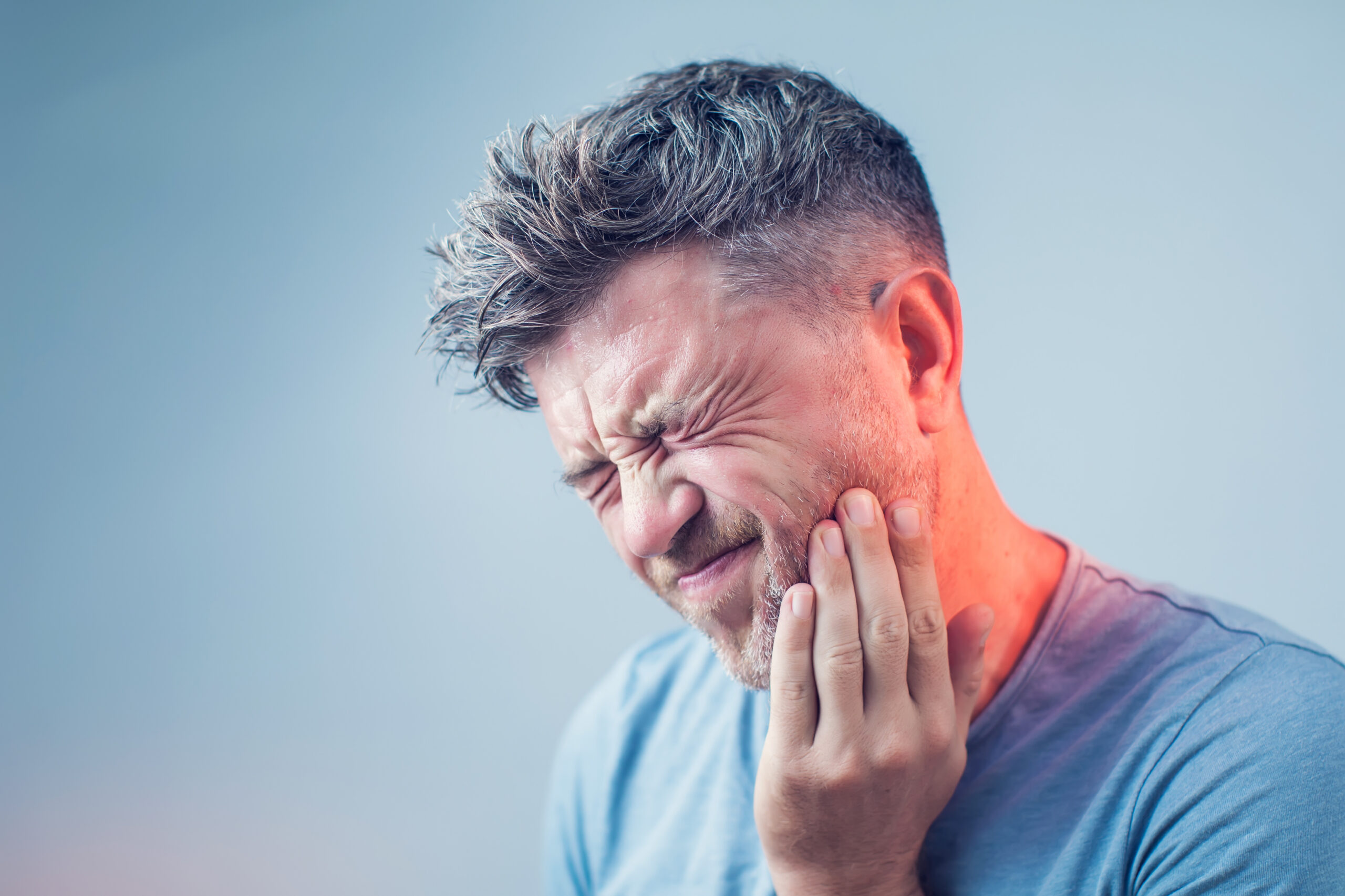 A man is experiencing toothache, signified by a reddened area on the side of his face